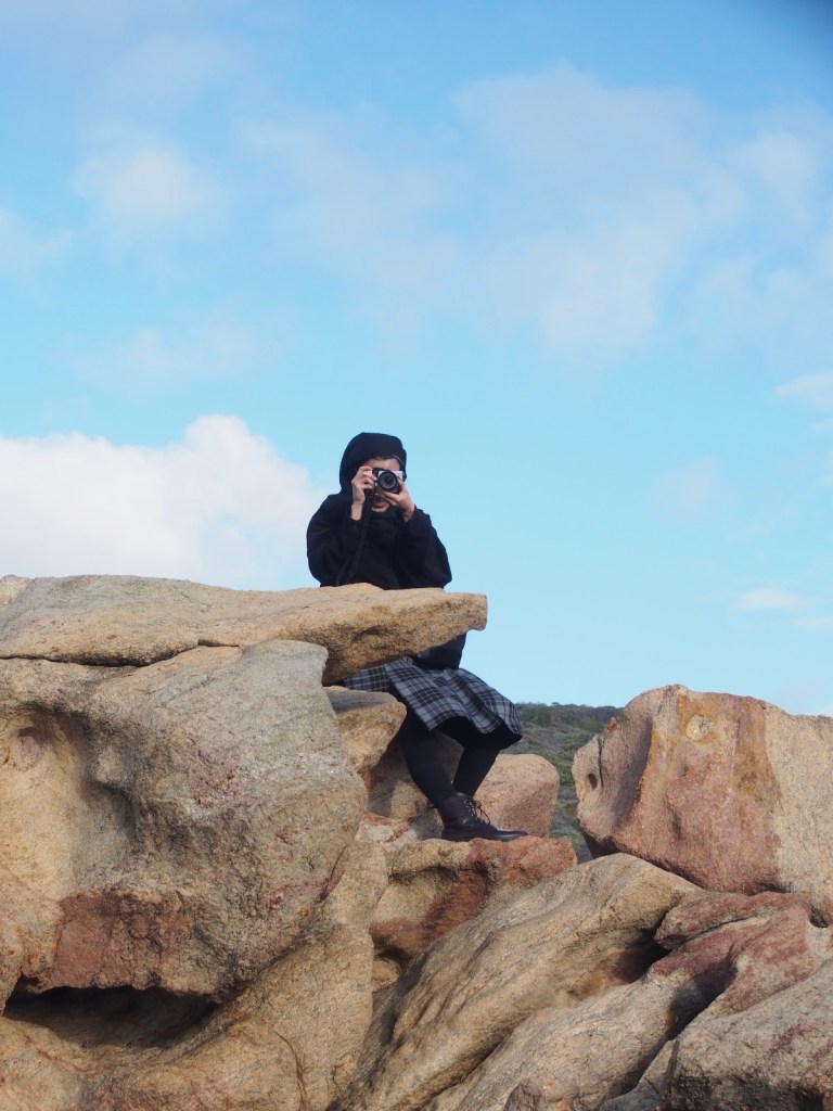 Photo of me sitting on a pile of boulders with a camera.